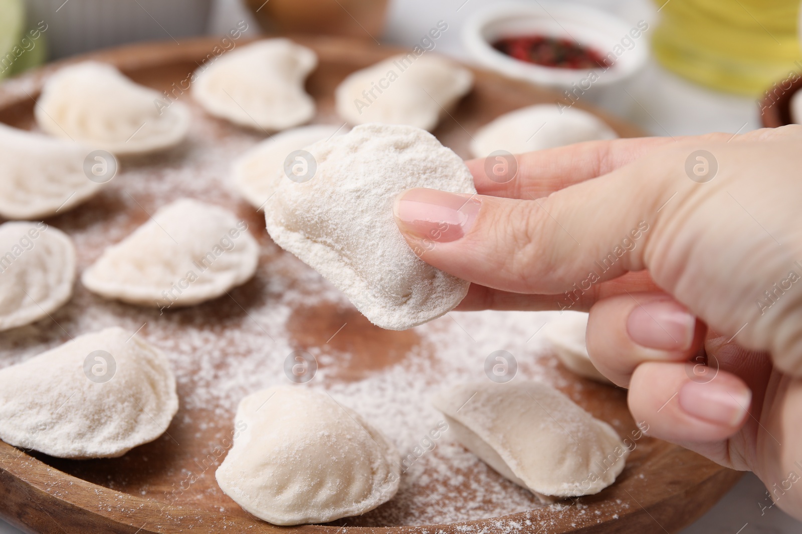 Photo of Woman holding raw dumpling (varenyk) with tasty filling at wooden board, closeup