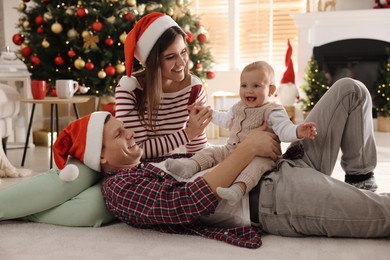 Photo of Happy family with cute baby on floor in room decorated for Christmas