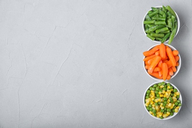 Photo of Bowls with frozen vegetables on grey background, top view. Product preservation