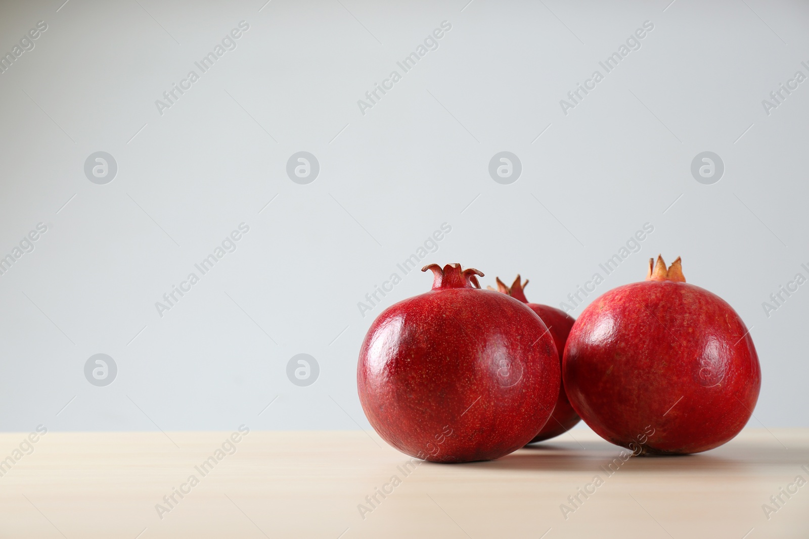 Photo of Ripe pomegranates on table against light background, space for text