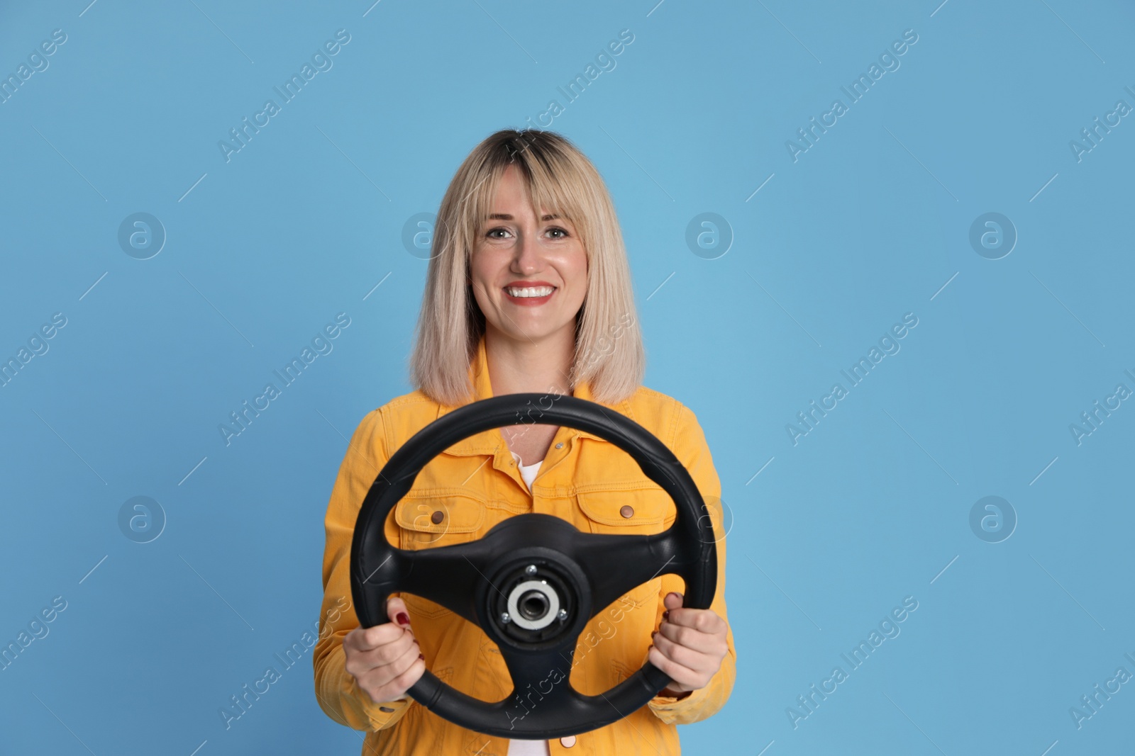 Photo of Happy woman with steering wheel on light blue background