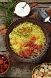 Photo of Delicious sauerkraut soup with smoked sausages and dill served on old wooden table, flat lay