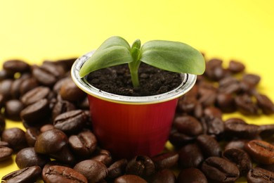 Photo of Coffee capsule with seedling and beans on yellow background, closeup