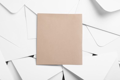 Blank brown card on pile of white paper envelopes, top view