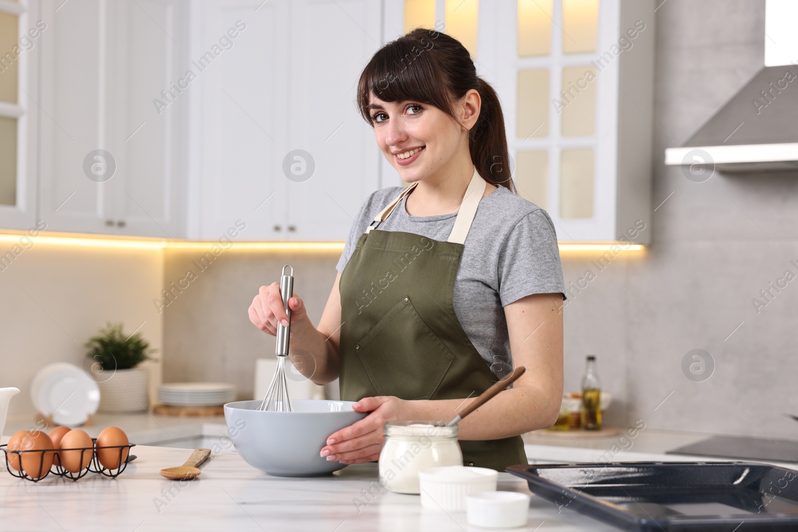 Photo of Happy young housewife mixing products into bowl at white marble table in kitchen