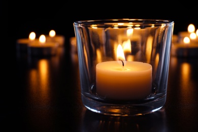 Photo of Wax candle burning on table in darkness, closeup