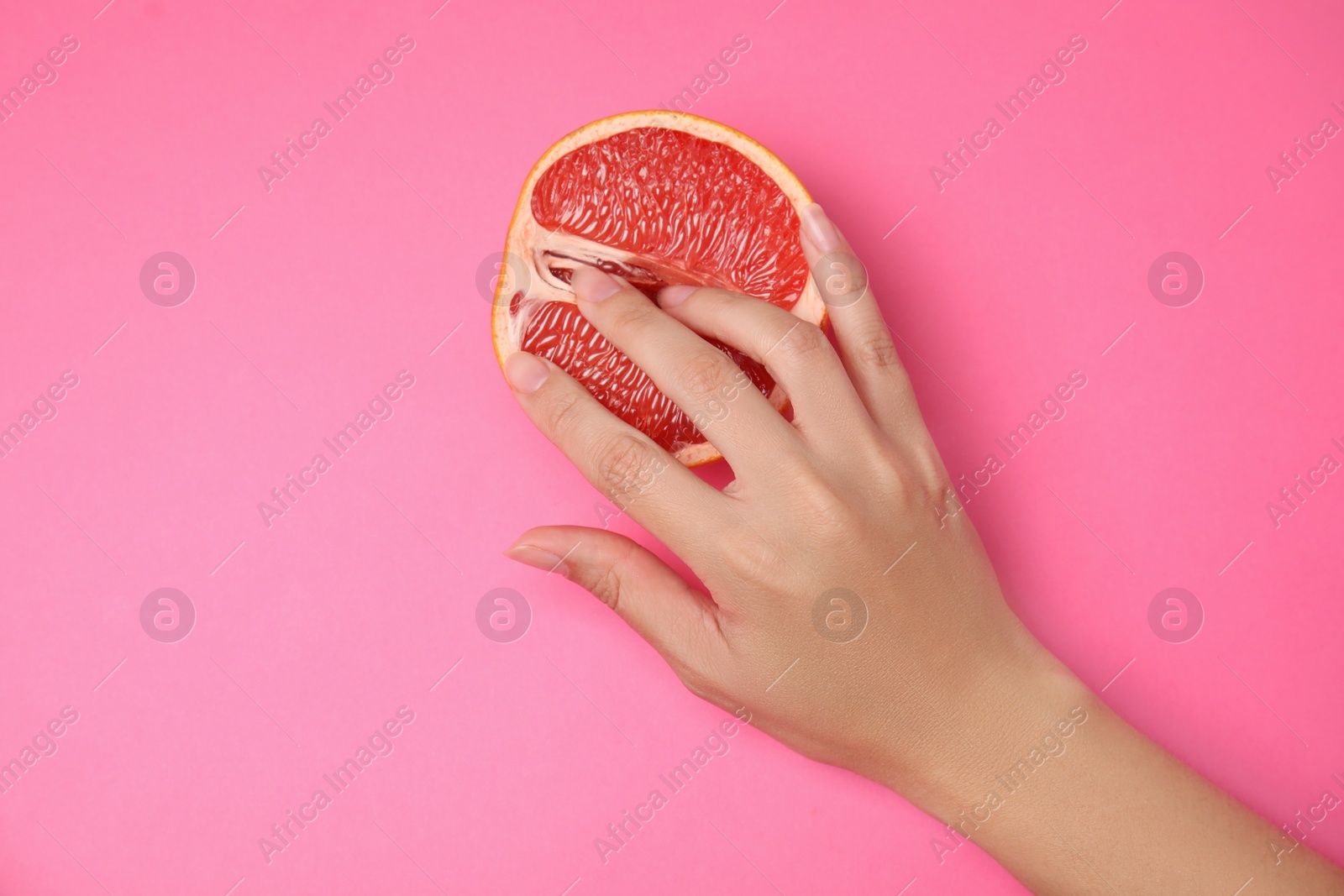 Photo of Young woman touching half of grapefruit on pink background, top view. Sex concept