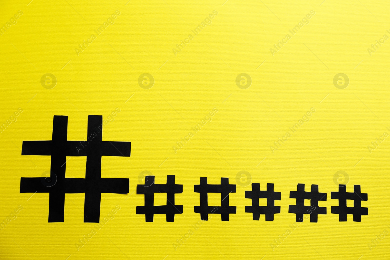 Photo of Black paper hashtag symbols on yellow background, flat lay. Space for text