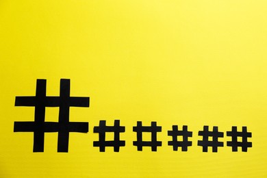 Photo of Black paper hashtag symbols on yellow background, flat lay. Space for text