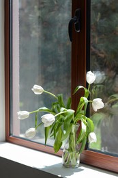 Photo of Bouquet of beautiful white tulip flowers in glass vase on windowsill indoors