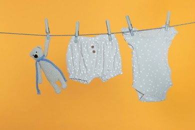 Photo of Baby clothes and bear toy drying on laundry line against orange background