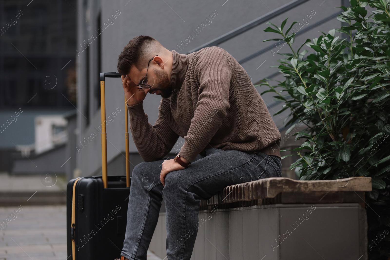 Photo of Being late. Frustrated man with suitcase sitting on bench outdoors