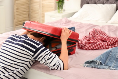Photo of Exhausted woman with her head inside of suitcase in bedroom