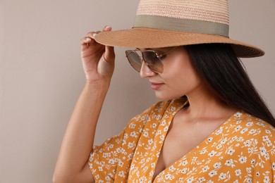 Beautiful young woman with straw hat and stylish sunglasses on beige background