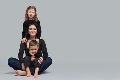 Photo of Little children with their mother on grey background. Space for text