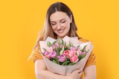 Happy young woman with bouquet of beautiful tulips on yellow background