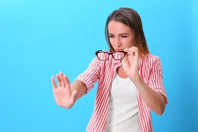 Young woman with vision problem wearing glasses on blue background