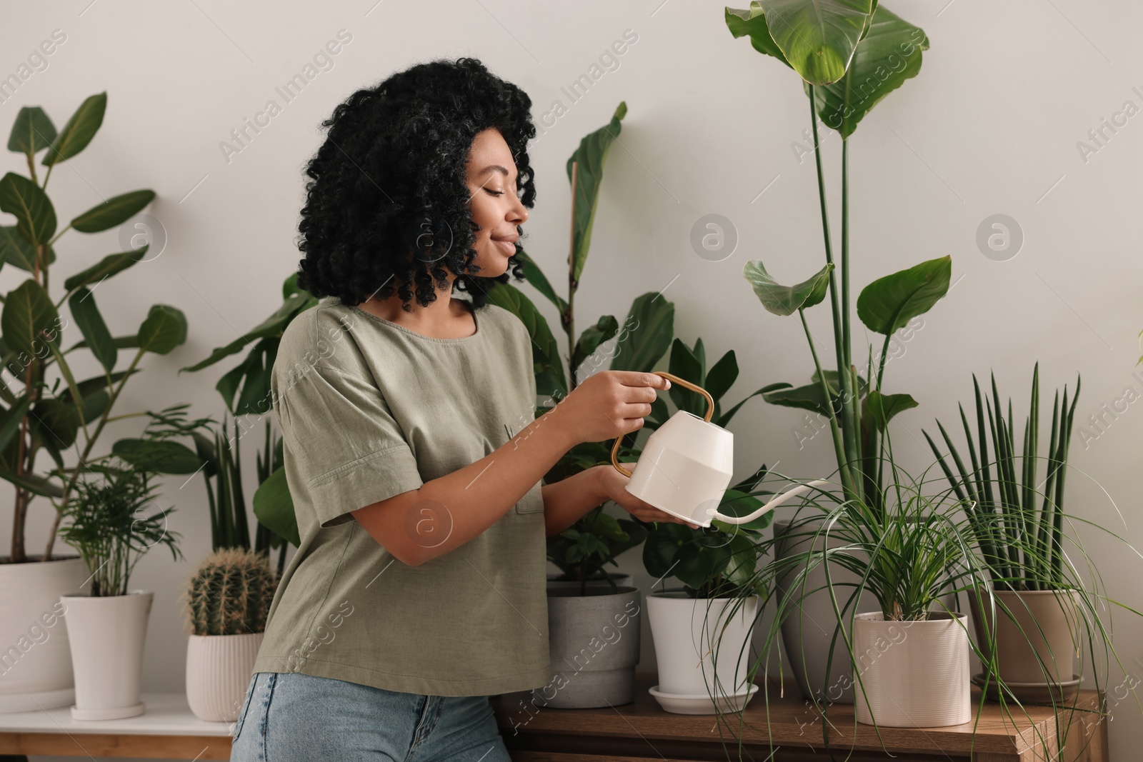 Photo of Happy woman watering beautiful potted houseplants indoors