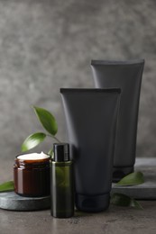 Facial cream and other men's cosmetic with green leaves on grey stone table. Mockup for design