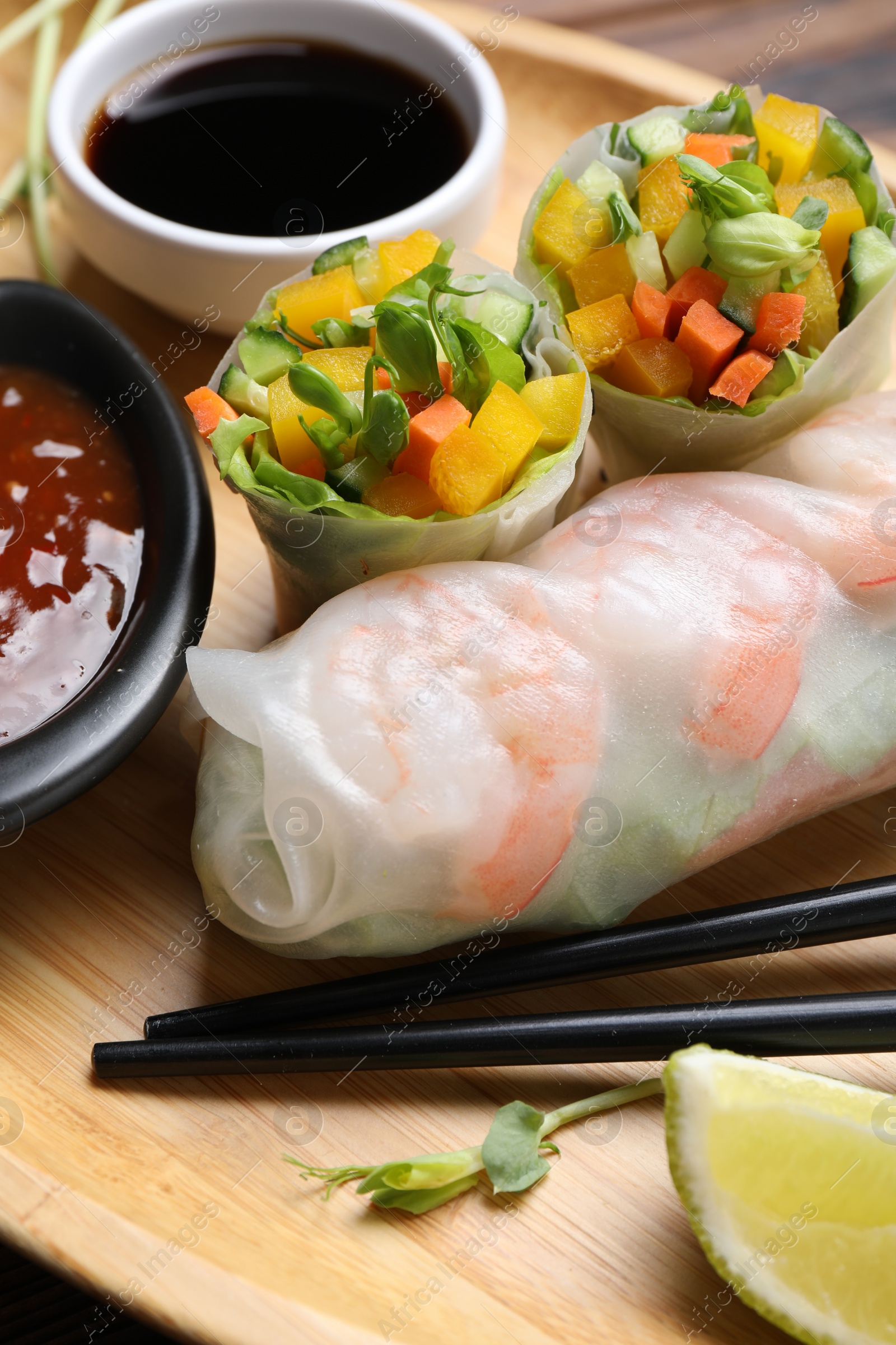 Photo of Tasty spring rolls and sauces on wooden plate, closeup