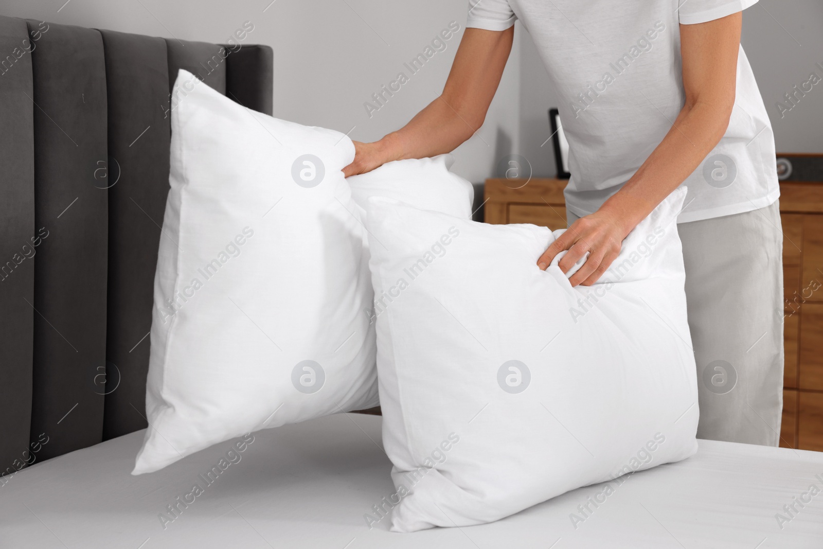 Photo of Woman putting pillows on bed at home, closeup. Space for text