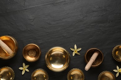 Photo of Flat lay composition with golden singing bowls on black table. Space for text