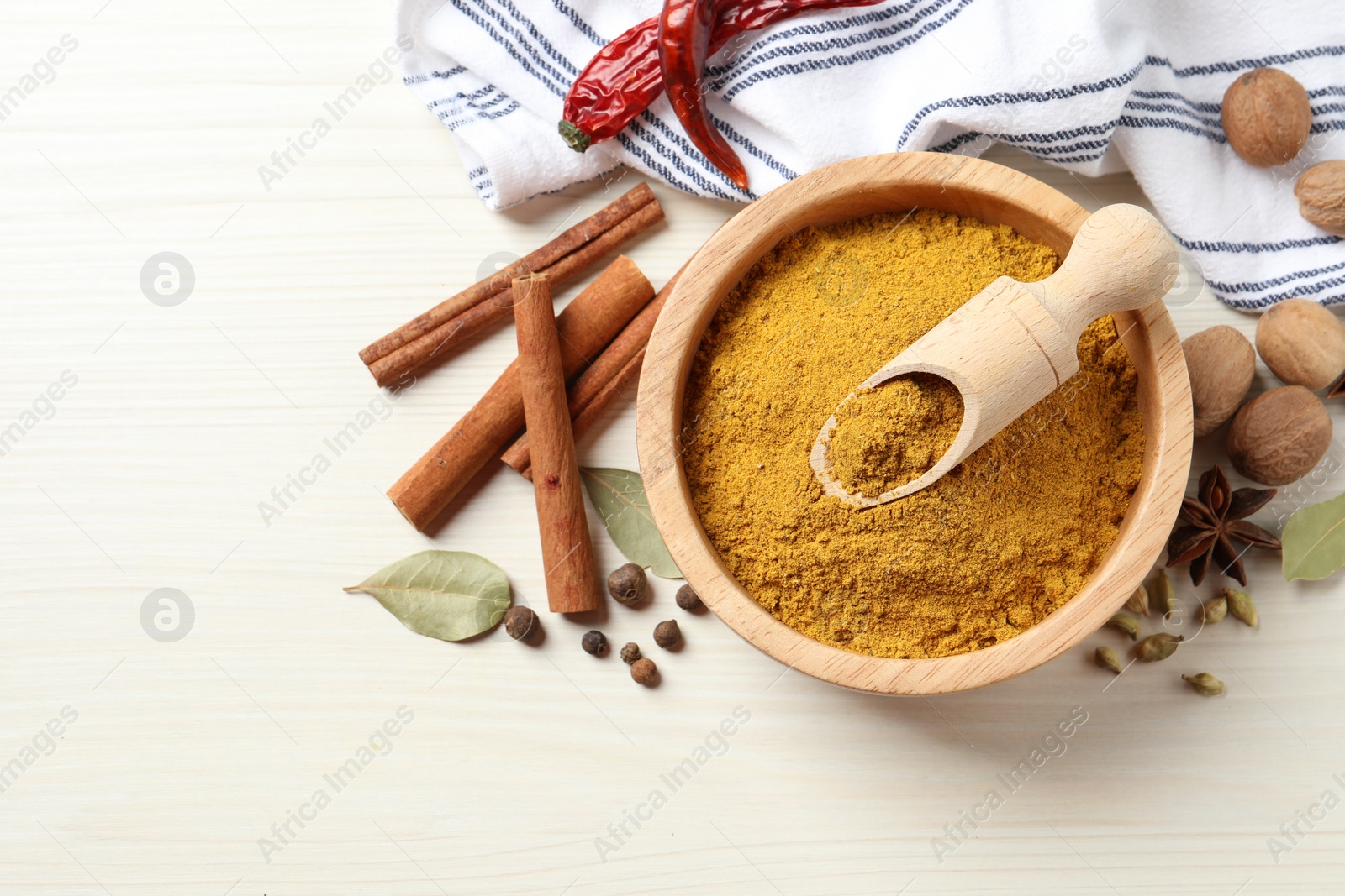 Photo of Dry curry powder in bowl and other spices on light wooden table, flat lay. Space for text