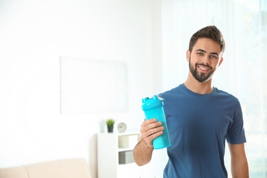 Photo of Young man with bottle of protein shake at home. Space for text