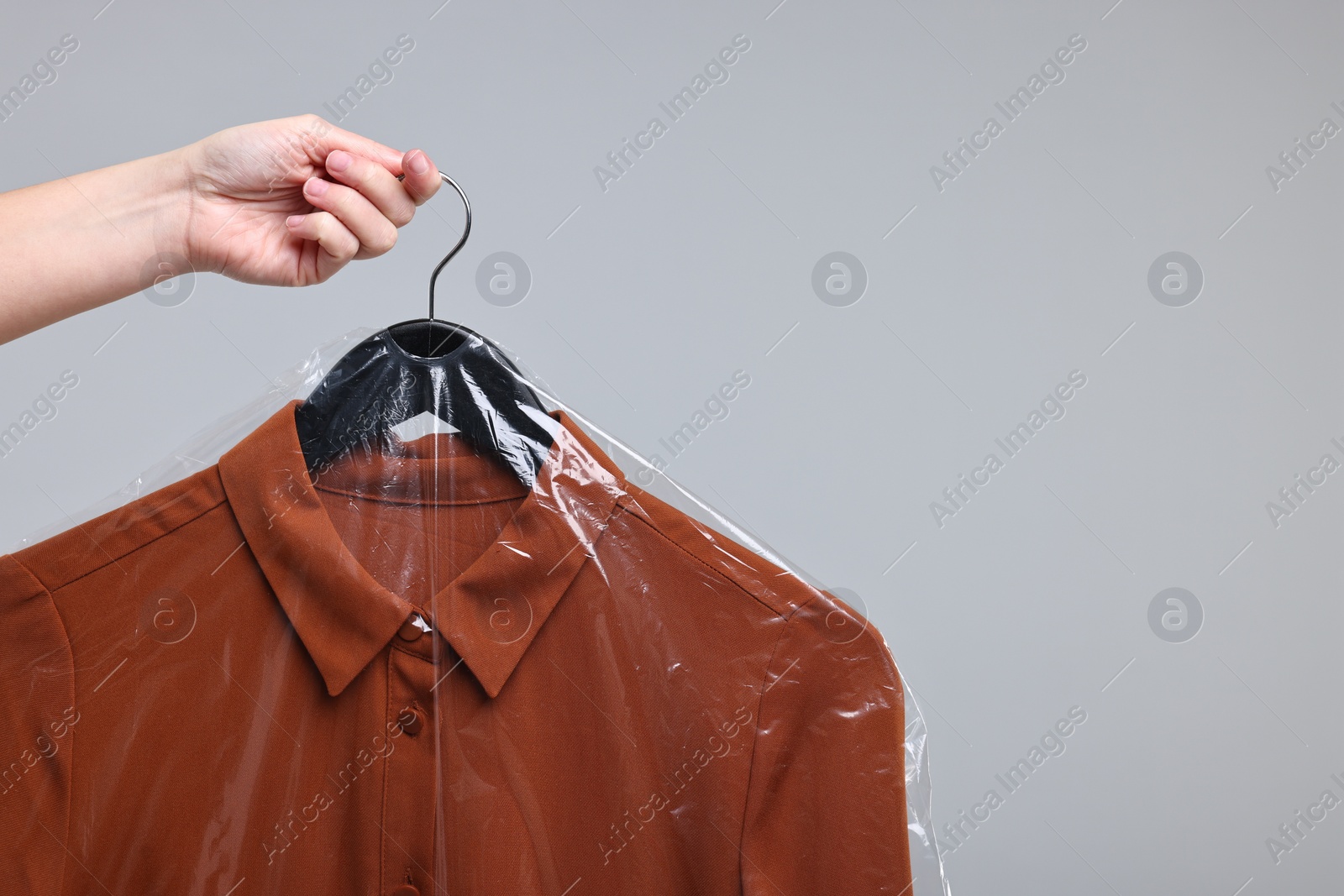 Photo of Dry-cleaning service. Woman holding shirt in plastic bag on gray background, closeup. Space for text