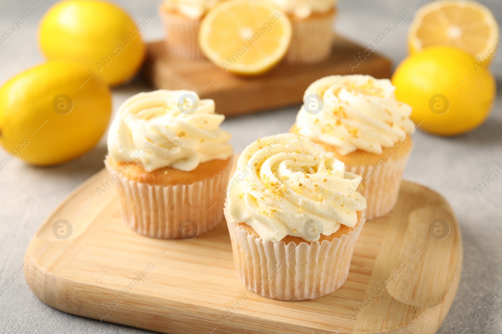 Photo of Tasty cupcakes with cream, zest and lemons on light grey table