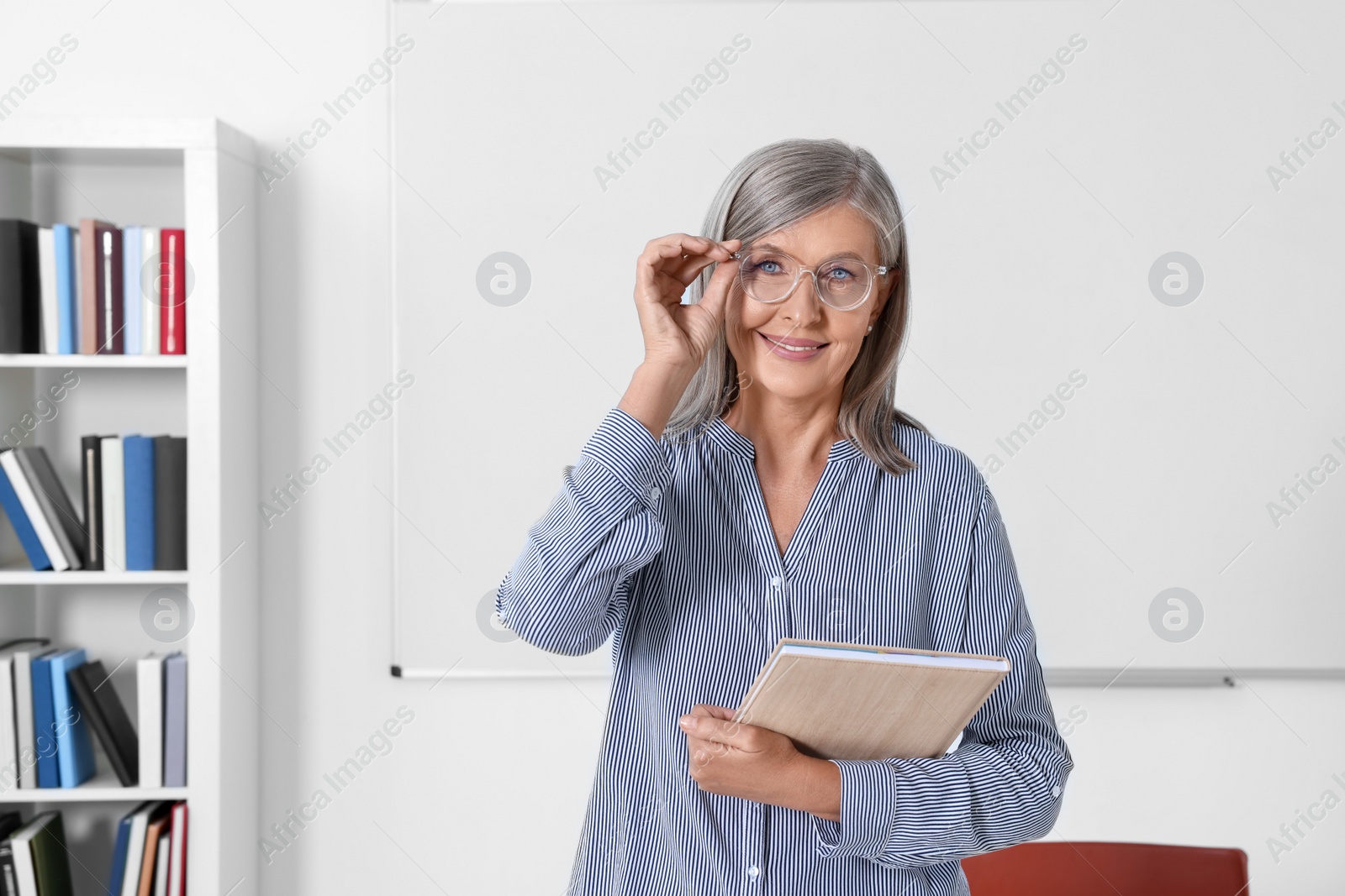 Photo of Portrait of professor with notebook near whiteboard in classroom, space for text