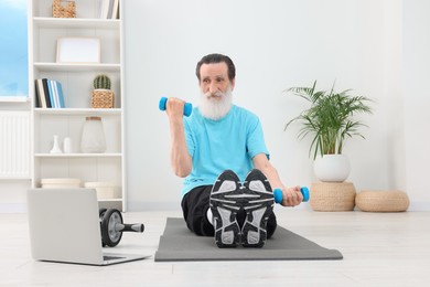 Photo of Senior man exercising with dumbbells while watching online tutorial at home. Sports equipment