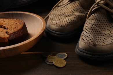 Poverty. Old shoes, pieces of bread and coins on wooden table, closeup