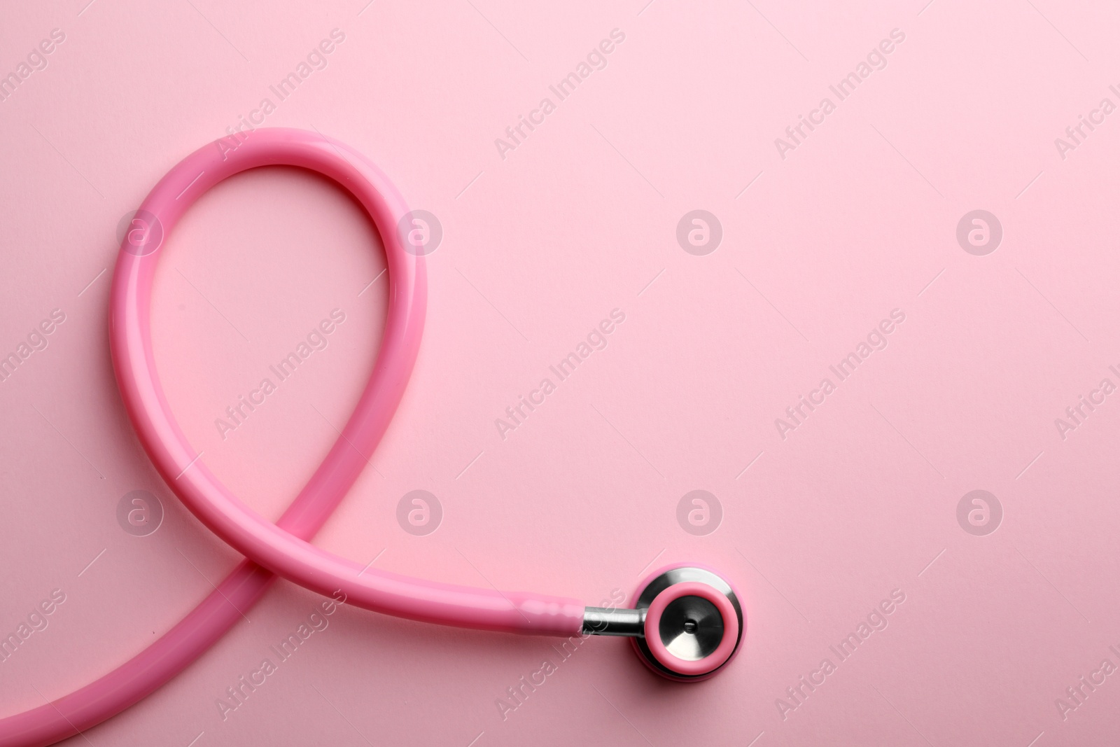 Photo of Pink stethoscope folded like awareness ribbon on color background, top view with space for text. Breast cancer concept