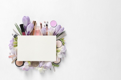 Makeup products, spring flowers and blank card on white background, top view. Space for text