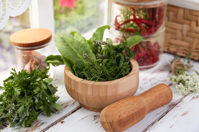 Photo of Mortar with pestle and fresh green herbs on white wooden table near window