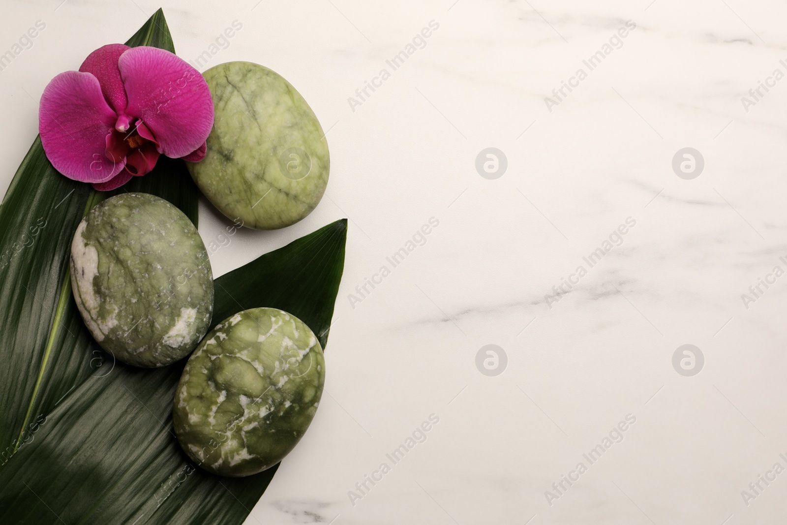 Photo of Beautiful spa composition with stones, flower and leaves on white marble table, flat lay. Space for text