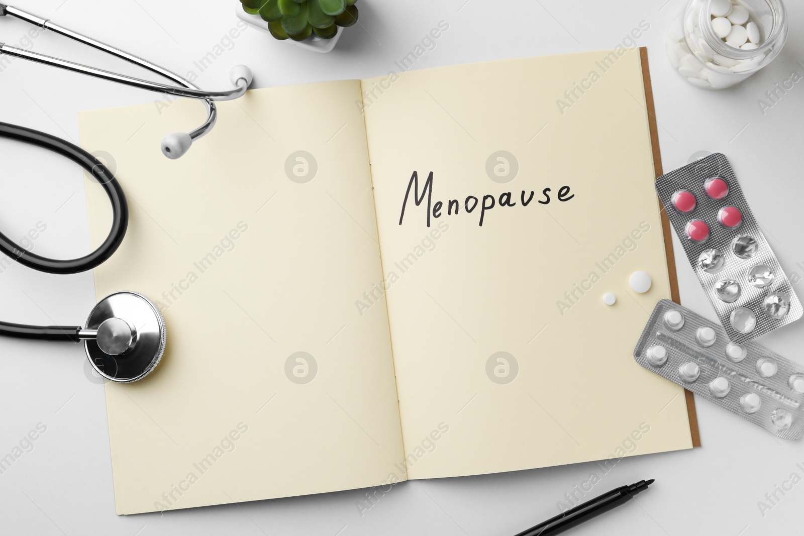 Photo of Notebook with word Menopause, pills and stethoscope on white table, flat lay