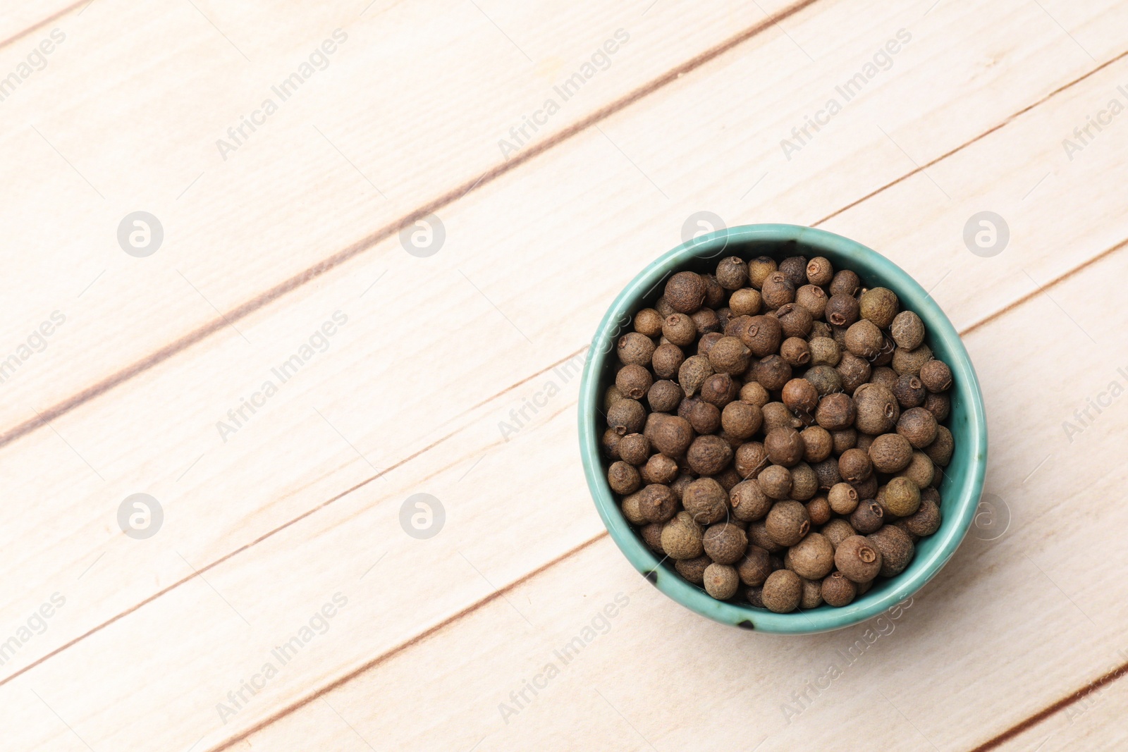 Photo of Dry allspice berries (Jamaica pepper) in bowl on light wooden table, top view. Space for text