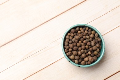 Dry allspice berries (Jamaica pepper) in bowl on light wooden table, top view. Space for text