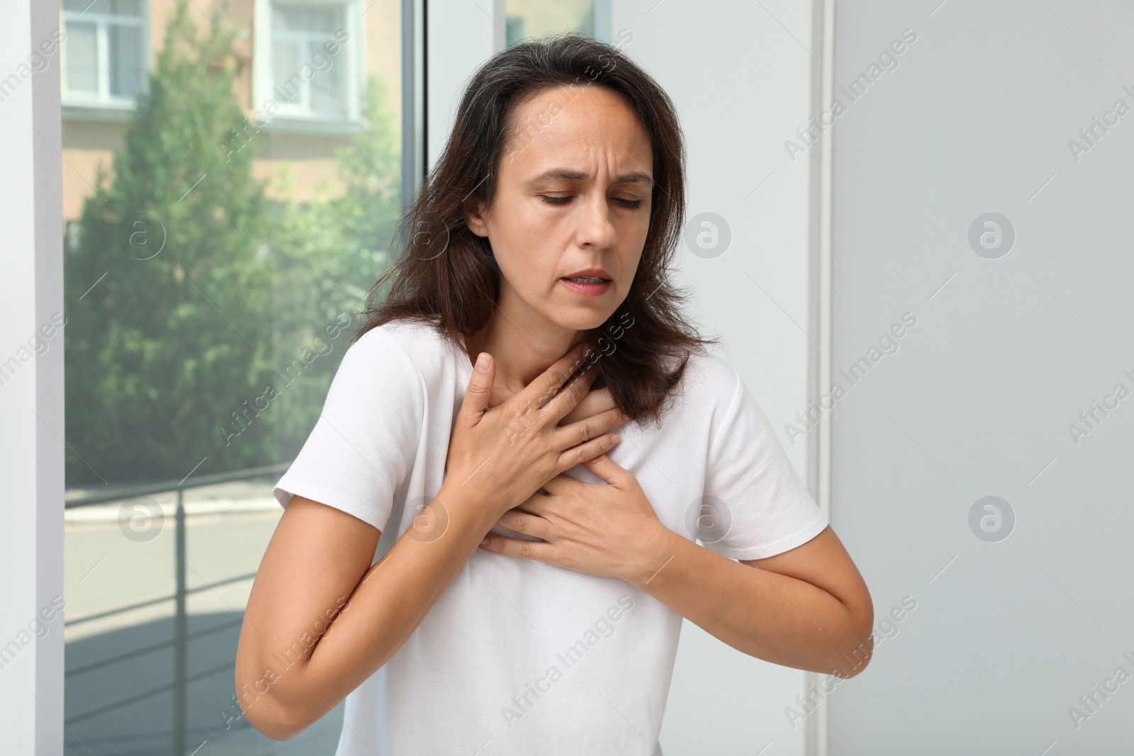 Photo of Mature woman suffering from breathing problem near window indoors