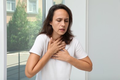 Photo of Mature woman suffering from breathing problem near window indoors