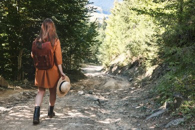 Photo of Woman with backpack and hat walking in forest, back view