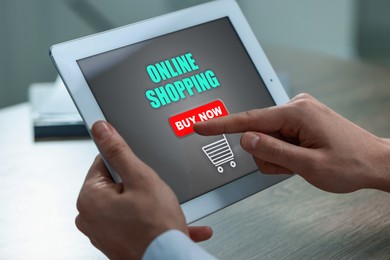 Man using tablet for online shopping at wooden table, closeup