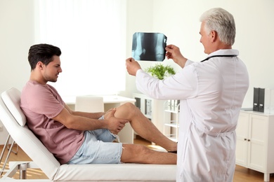 Photo of Senior doctor with X-ray and young patient in clinic. Knee problem