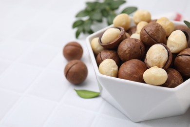 Tasty Macadamia nuts in bowl on white table, closeup. Space for text
