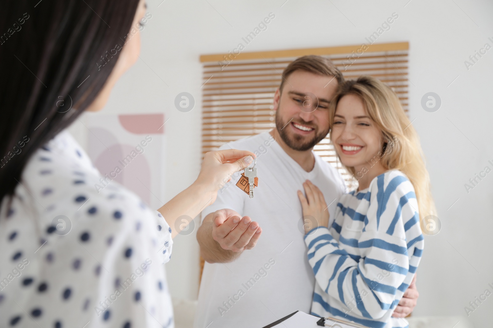 Photo of Real estate agent giving key to happy young couple in new house, focus on hands