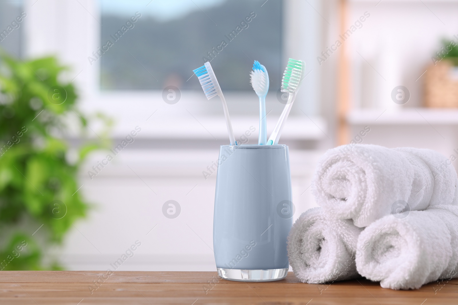 Photo of Plastic toothbrushes in holder and towels on wooden table. Space for text