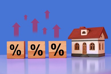 Image of Mortgage rate rising illustrated by upward arrows and percent signs. House model and wooden cubes on table