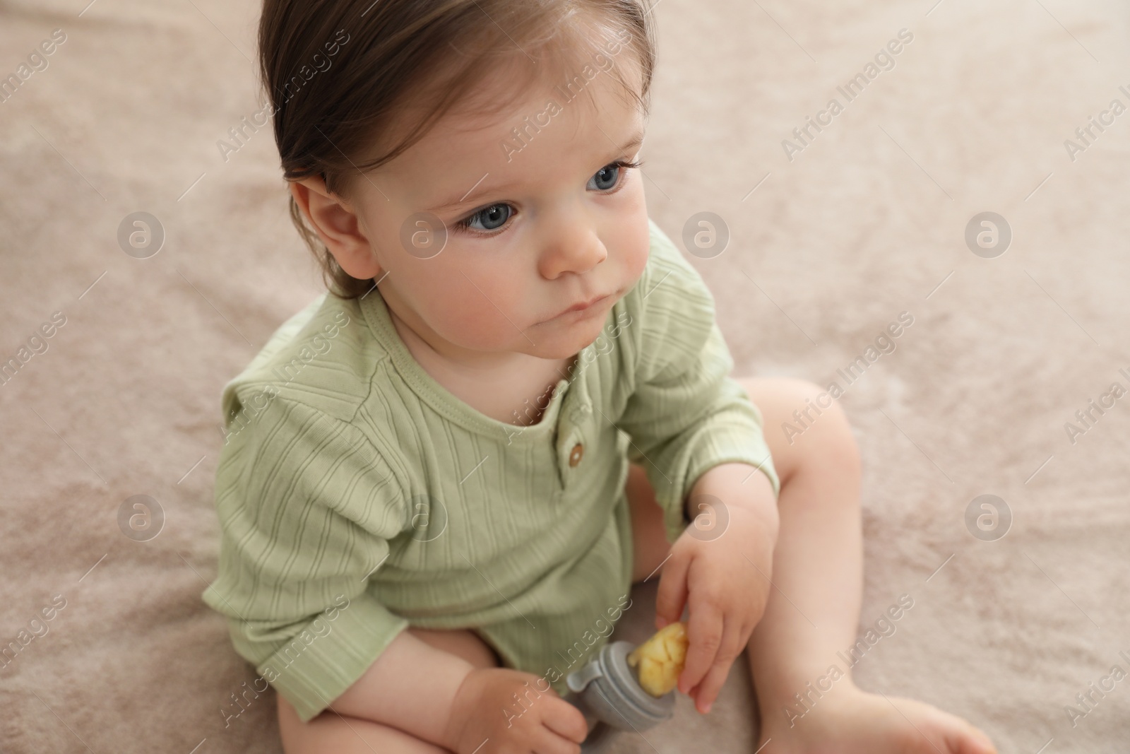 Photo of Cute baby girl with nibbler on beige blanket